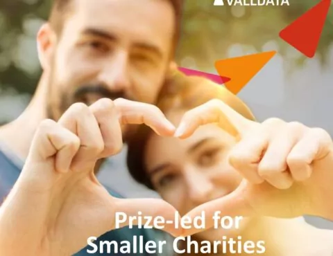 Couple forming hand loveheart with their fingers with Woods Valldata branding in the background and the words Prize-led for smaller charities webinar 2026 written below